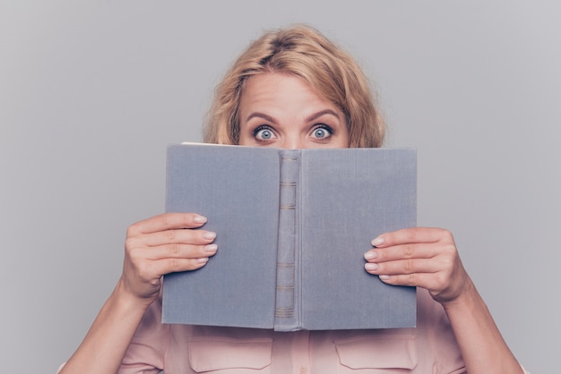 Close up portrait of blonde girl hold book hide her face isolated on gray