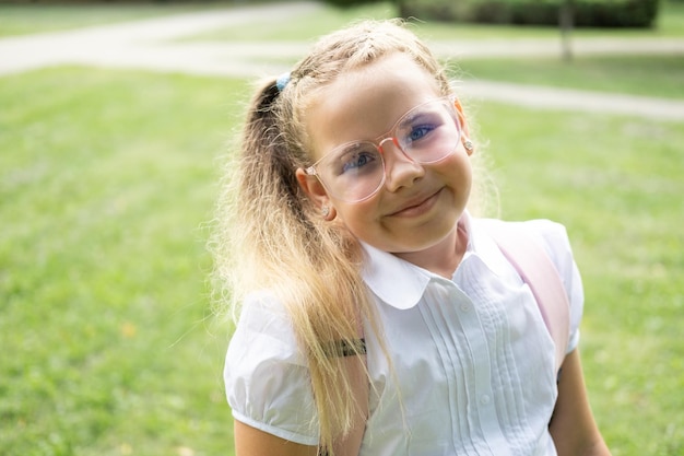 close up portrait of blonde schoolgirl in glasses white shirt with pink backpack back to school