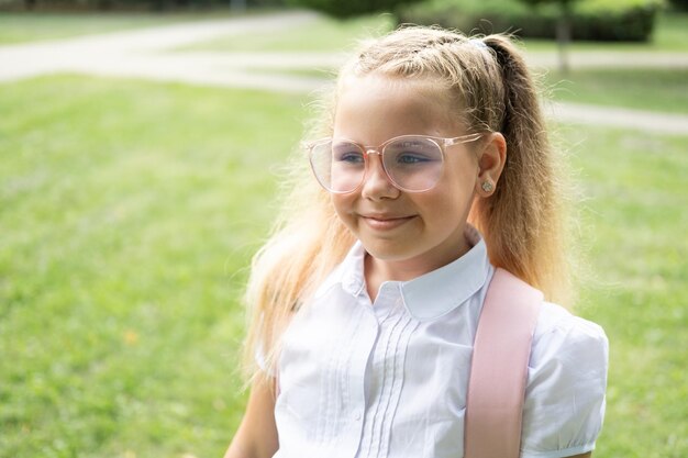 close up portrait of blonde schoolgirl in glasses white shirt with pink backpack back to school