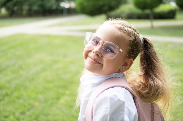 close up portrait of blonde schoolgirl in glasses white shirt with pink backpack back to school