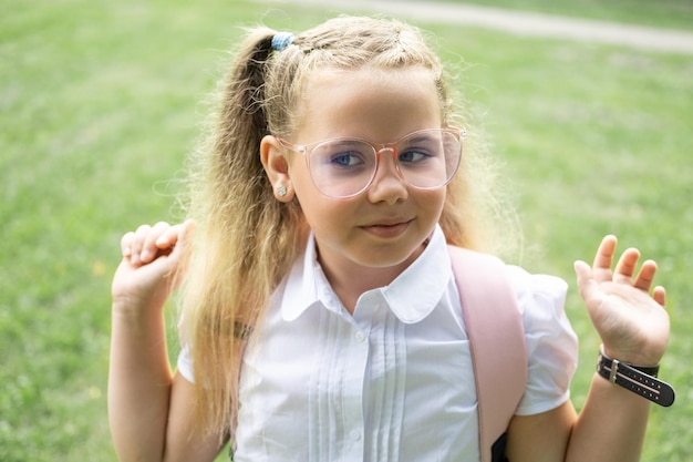 close up portrait of blonde schoolgirl in glasses white shirt with pink backpack back to school