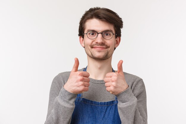 Photo close-up portrait of cheerful enthusiastic male employee agrees with coworker, show thumbs-up and smiling pleased, give approval, guarantee best quality of coffee, stand