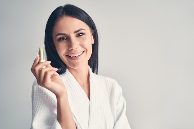 Close up portrait of a cheerful lady demonstrating a cosmetic product in front of the front