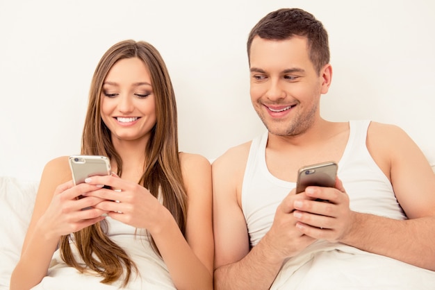 Close up portrait of cheerful smiling couple reading sms on phones