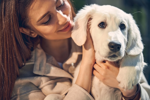 Close up portrait of a contented dark-haired young Caucasian female owner looking at her cute pet