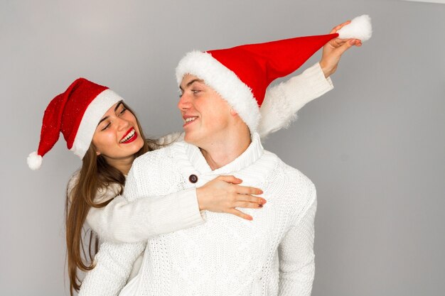 Photo close up portrait of couple in love celebrates christmas and having fun in santa hats in studio on gray background