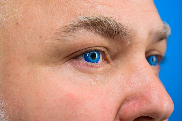 Close up portrait of crying bearded man through hole in blue paper sad emotions cry tears discount