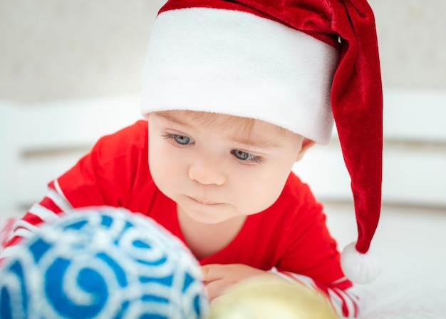 Close up portrait of cute caucasian baby wearing santa hat christmas balls in the foreground new