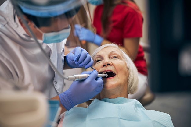 Close up portrait of doctor wearing professional uniform and equipment in work while caring at the teeth of patient in medicine clinic