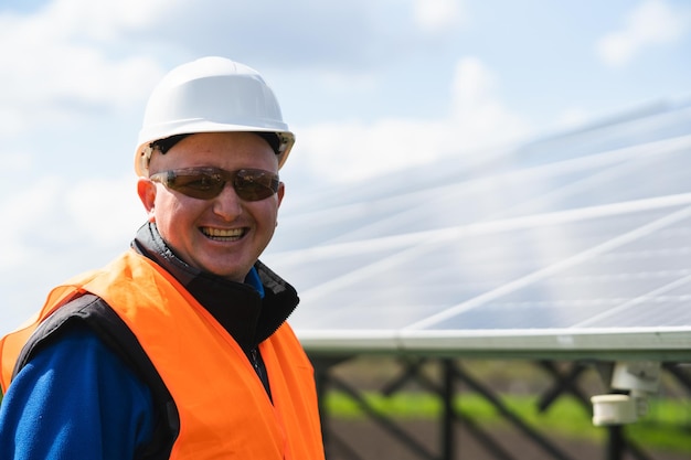 Close up portrait of engineer in hard hat and protective glasses on farm with solar panels