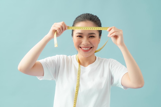 Close up portrait of an excited young girl looking at a measuring tape isolated over blue background