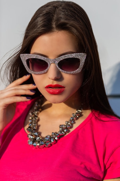 Close up portrait of fashionable brunette woman in stylish sunglasses and pink t-shirt