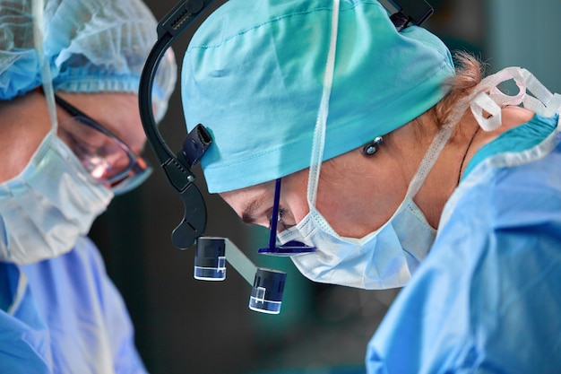 Close up portrait of female surgeon doctor wearing protective mask and hat during the operation. Healthcare, medical education, surgery concept.