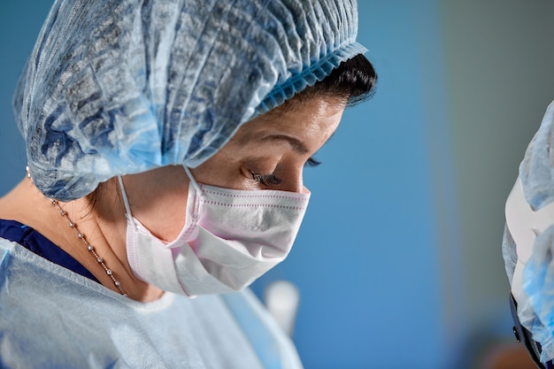 Close up portrait of female surgeon doctor wearing protective mask and hat during the operation.