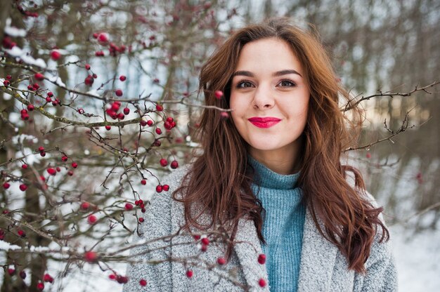 Close up portrait of gentle girl in gray coat near the branches of a snow-covered tree.