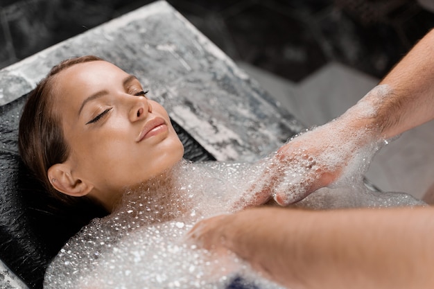 Close-up portrait of girl on foam peeling procedures in spa. Model is relaxing in Turkish hammam.