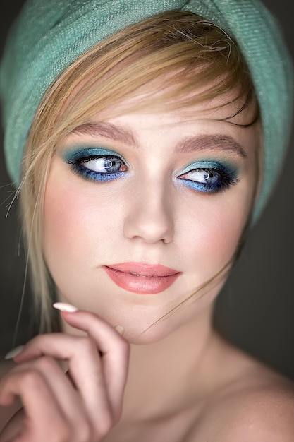 Close-up portrait of a girl with blue makeup and a hat on her head.