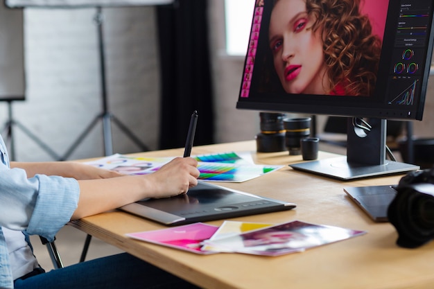 Close up portrait of graphic designer hands retouching images using graphic drawing tablet in special program.