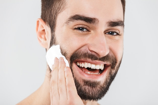 Close up portrait of a handsome bearded man standing isolated over white, applying shaving foam