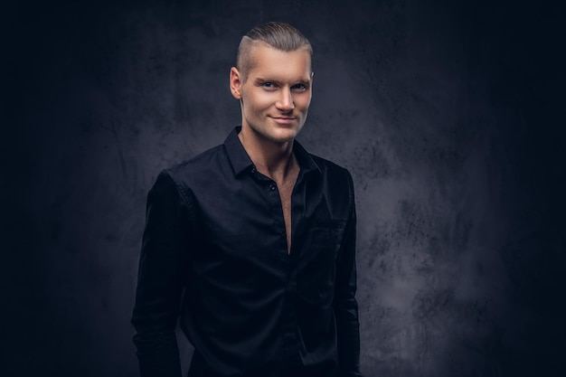 Close-up, a portrait of a handsome man in black shirt poses against a dark background, standing in the studio.