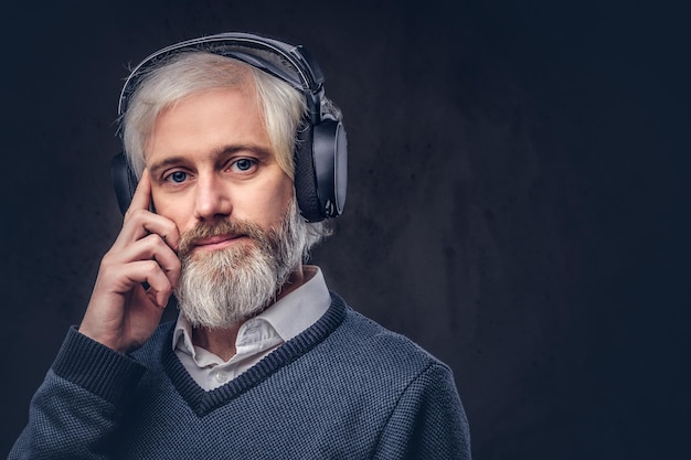 Close-up portrait of a handsome senior man listening to music in headphones. Isolated a dark background.