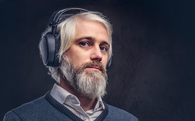 Close-up portrait of a handsome senior man listening to music in headphones. Isolated a dark background.