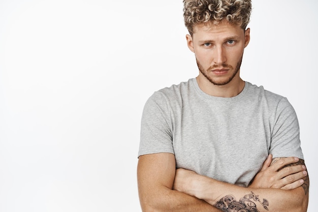 Close up portrait of handsome stylish blond man cross arms on chest looking confident and sassy at camera standing serious against white background