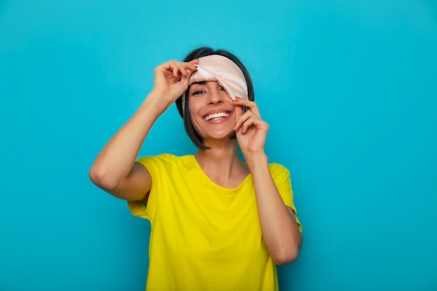 Close up portrait of happy young beautiful woman in mask for dream on her eyes while she preparing for nap and looking from under mask on camera