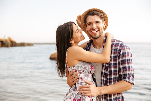 Close up portrait of a happy young hipster couple in love standing at the beach and hugging