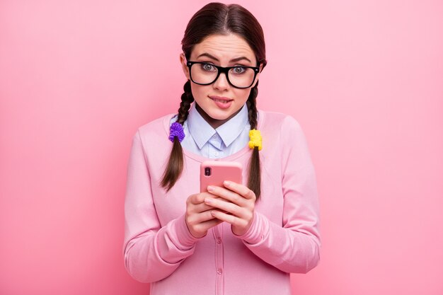 Close-up portrait of her she attractive pretty lovely cute unsure shy brown-haired girl geek using digital device 5g app choosing buying goods service biting lip isolated pink pastel color background