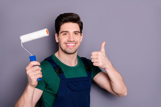 Close-up portrait of his he nice attractive brunette cheerful cheery glad guy making renovation new design holding in hand roller showing thumbup isolated over gray pastel color wall