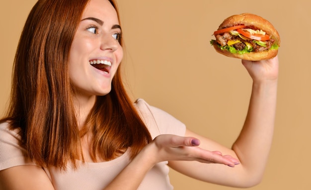 Close up portrait of a hungry young woman eating burger isolated over nude background