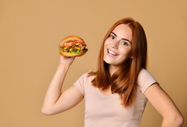 Close up portrait of a hungry young woman eating burger isolated over nude background