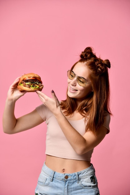 Close up portrait of a hungry young woman eating burger isolated over white background