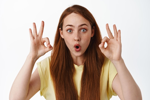 Close up portrait of impressed modern girl gasp amazed, drop jaw and say wow, show okay signs to praise and compliment awesome thing, white background.