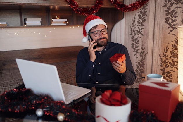 Close up portrait of joyful Caucasian handsome man in santa hat sitting in cozy room