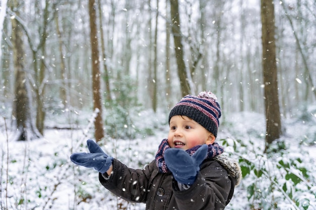 Close up portrait of a little boy playing with snowflakes in a park in winter. Happy child enjoys the first snow in a forest. Waiting for Christmas.3