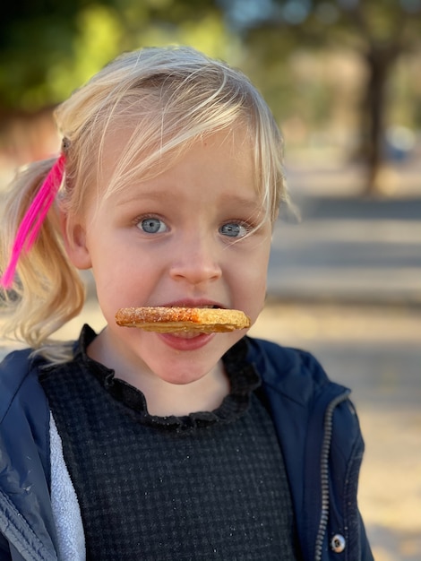 Close-up portrait of a lovely fair-haired girl looking funny with a biscuit in the teeth.