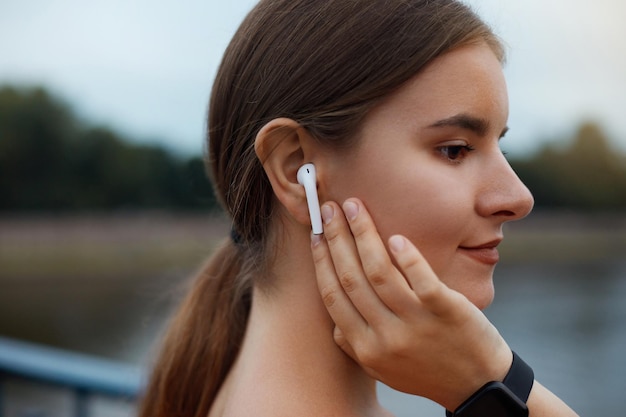 Close up portrait of a lovely young fitness girl listening to music through wireless earphones