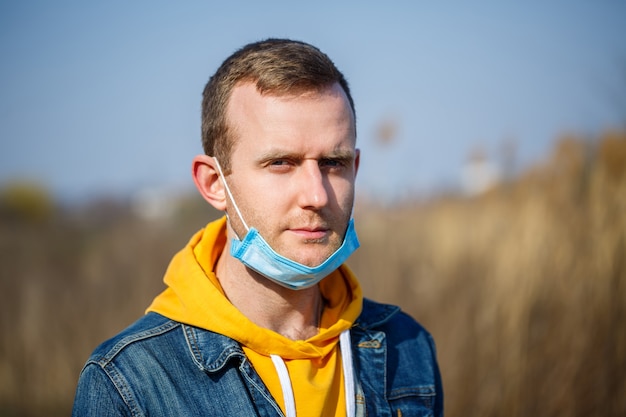 Close up portrait of a man outdoor in a surgical mask with rubber ear straps. Typical three-layer surgical mask for covering the mouth and nose. Bacteria mask procedure. Protection concept.