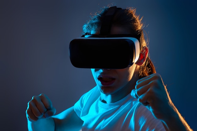 Close-up portrait of man using glasses of virtual reality on dark blue background. Neon light.