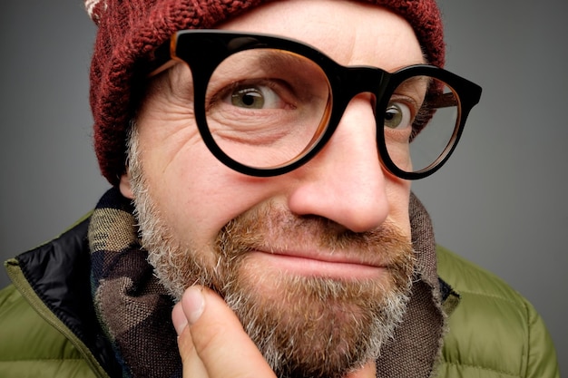 Close up portrait of middle aged europeam man in funny warm hat and glasses noticing hidden camera