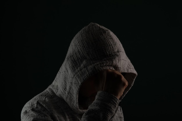 Close up portrait of mysterious man wearing sunglasses and hooded sweatshirt covering head with hands on face