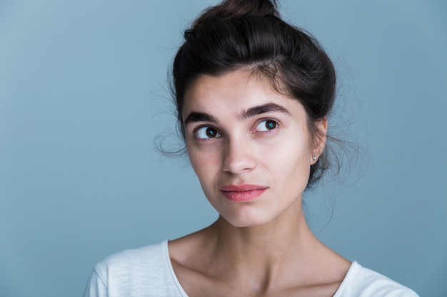 Close up portrait of a pensive unsatisfied pretty young brunette woman wearing white t-shirt standing isolated over blue background