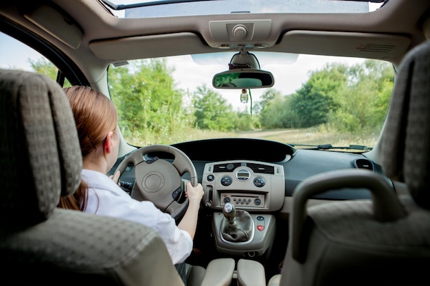 Close up portrait of pleasant looking female with glad positive expression being satisfied with unforgettable journey by car sits on driver s seat People driving transport concept