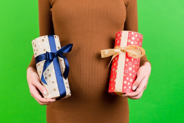 Close up portrait of pregnant woman in brown dress holding two gift boxes at green background Waiting for a baby boy or a baby girl Expecting twins Copy space