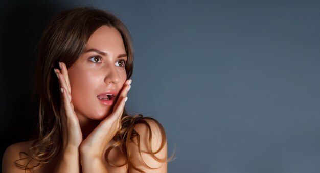 Close-up portrait pretty young woman scared with her hands to her face against dark isolated background