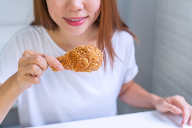 Close up portrait of a satisfied pretty Asian woman eating fried chicken isolated