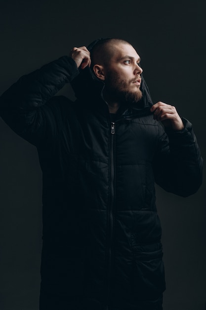 Close-up portrait of a serious young man in a jacket looking to the side on a gray space. bald with a beard