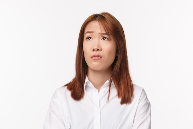 Close-up portrait of skeptical young asian girl grimacing aversion and judgemental looking left, raising eyebrow surprised and unimpressed with something unpleasant, stand white wall